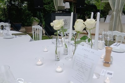 Table décorée pour un événement avec nappes blanches, roses blanches, bougies et menu imprimé.