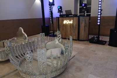 Deux trônes ornés de cristaux devant une table de DJ en bois éclairée par des projecteurs colorés.