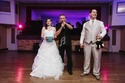 Un couple en tenue de mariage et un animateur sur une piste de danse dans une salle éclairée.