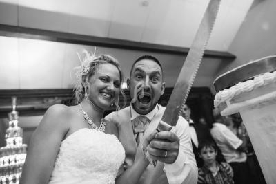 Un couple souriant coupe un gâteau de mariage avec une grande lame dans une ambiance festive.