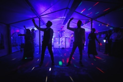 Des personnes dansent sous des lumières colorées dans une tente lors d'un événement festif en soirée.