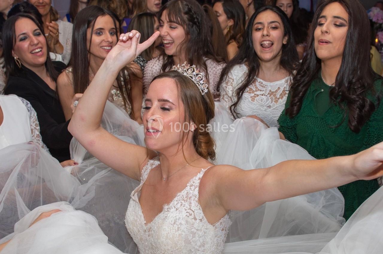 Une mariée en robe blanche danse joyeusement entourée d'invitées souriantes lors d'une célébration.