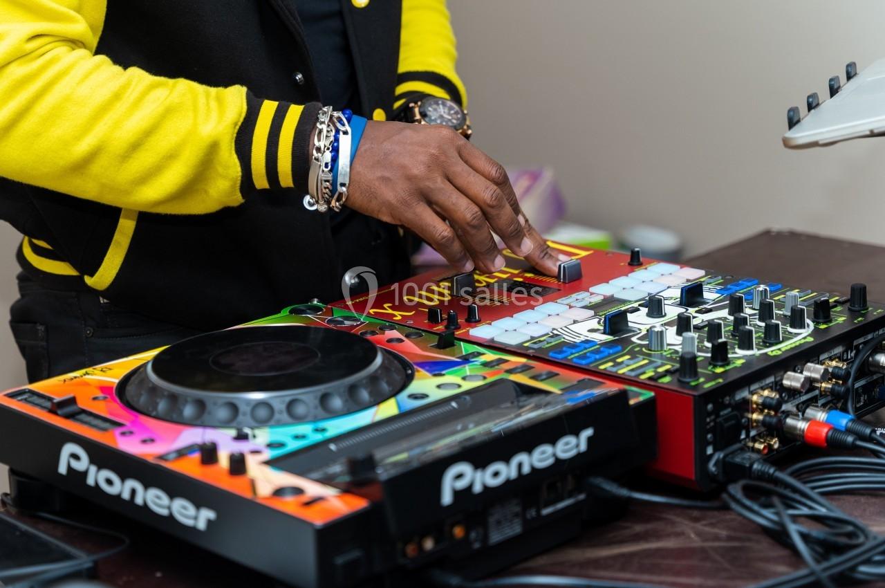 Un DJ ajuste les commandes d'une console de mixage colorée avec des équipements audio Pioneer sur une table.