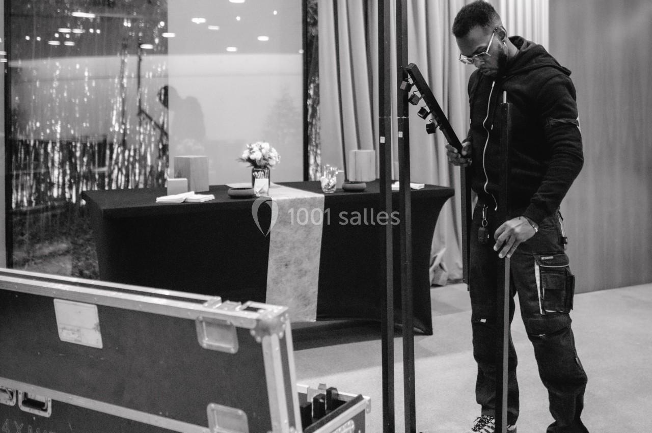 Un technicien installe un équipement dans une salle, avec une table décorée et une caisse de matériel au premier plan.