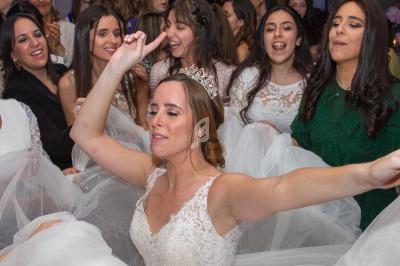 Une mariée souriante, portant une couronne, danse entourée d'invités en tenues festives.