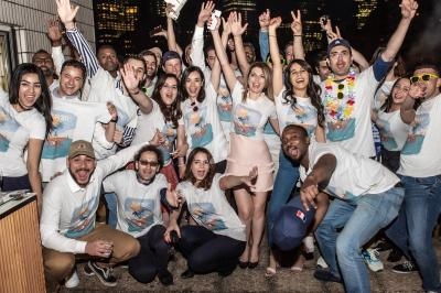Un groupe de personnes souriantes portant des t-shirts assortis posent ensemble lors d'un événement en extérieur le soir.