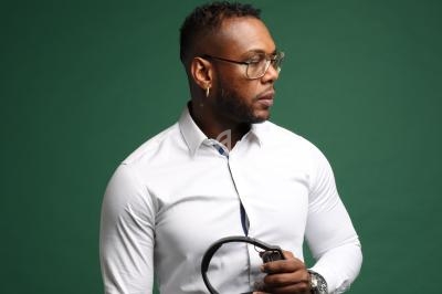 Homme portant une chemise blanche et des lunettes, tenant un casque audio dans un studio au fond vert.