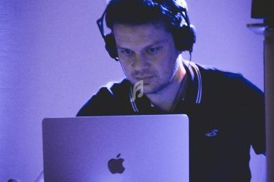 Un DJ portant un casque travaille sur un ordinateur portable dans une ambiance éclairée par des lumières bleues.