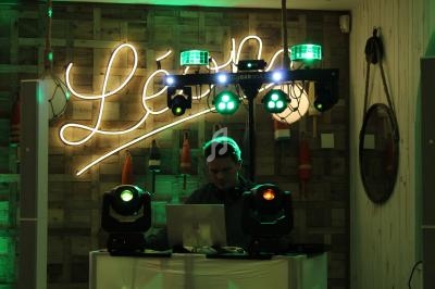Un DJ mixe sur son ordinateur portable, entouré de lumières colorées dans un décor en bois avec des bouées suspendues.
