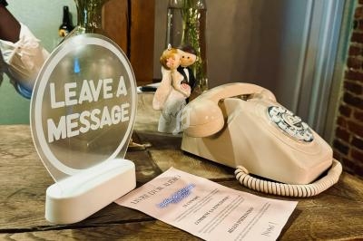 Téléphone vintage beige sur un comptoir en bois, accompagné d'un panneau ’Leave a message’ et d'un bouquet de fleurs.