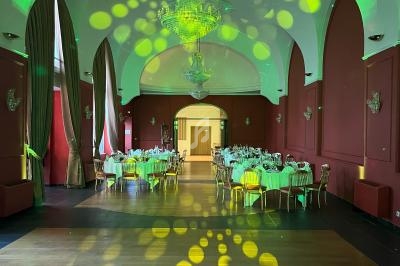 Salle de réception avec tables dressées, lustres suspendus et éclairage vert projeté au plafond et au sol.
