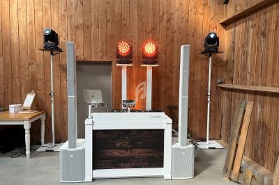 Installation de matériel de sonorisation et d'éclairage dans une salle en bois, avec une table de mixage au centre.