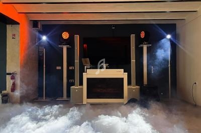 Console de DJ avec éclairage coloré et fumée au sol dans une salle moderne.