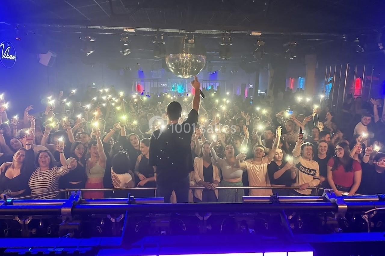 Un artiste sur scène face à une foule brandissant des téléphones allumés dans une salle de concert.
