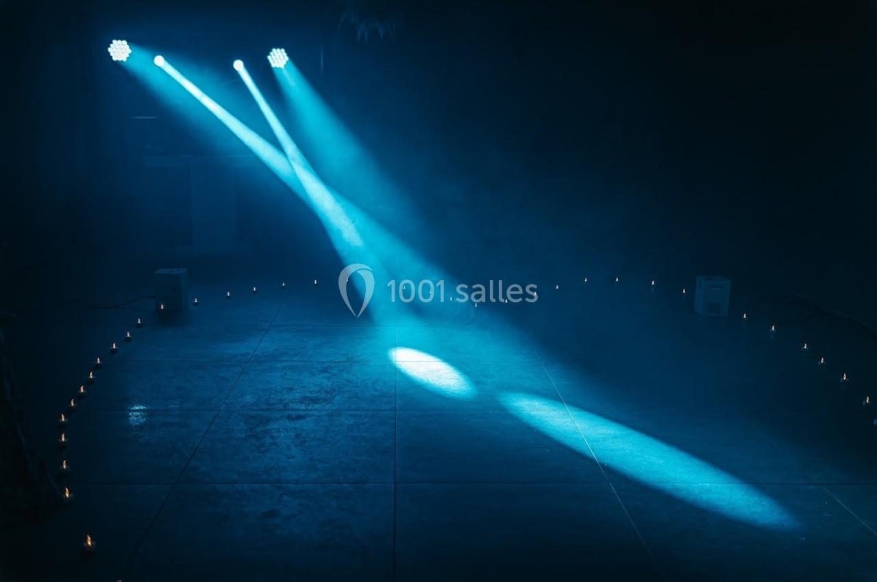 Deux faisceaux de lumière bleue éclairent un sol entouré de petites bougies dans une ambiance sombre et brumeuse.