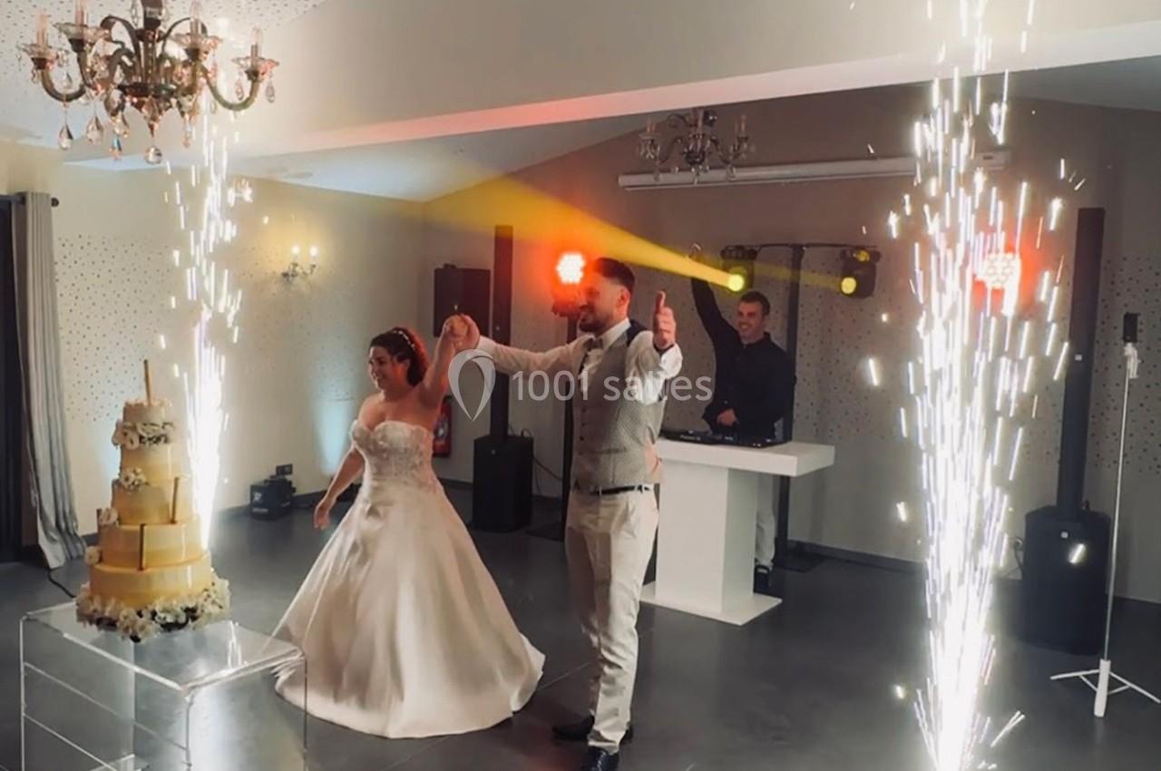 Un couple de mariés danse sous des étincelles près d'un gâteau de mariage dans une salle éclairée.