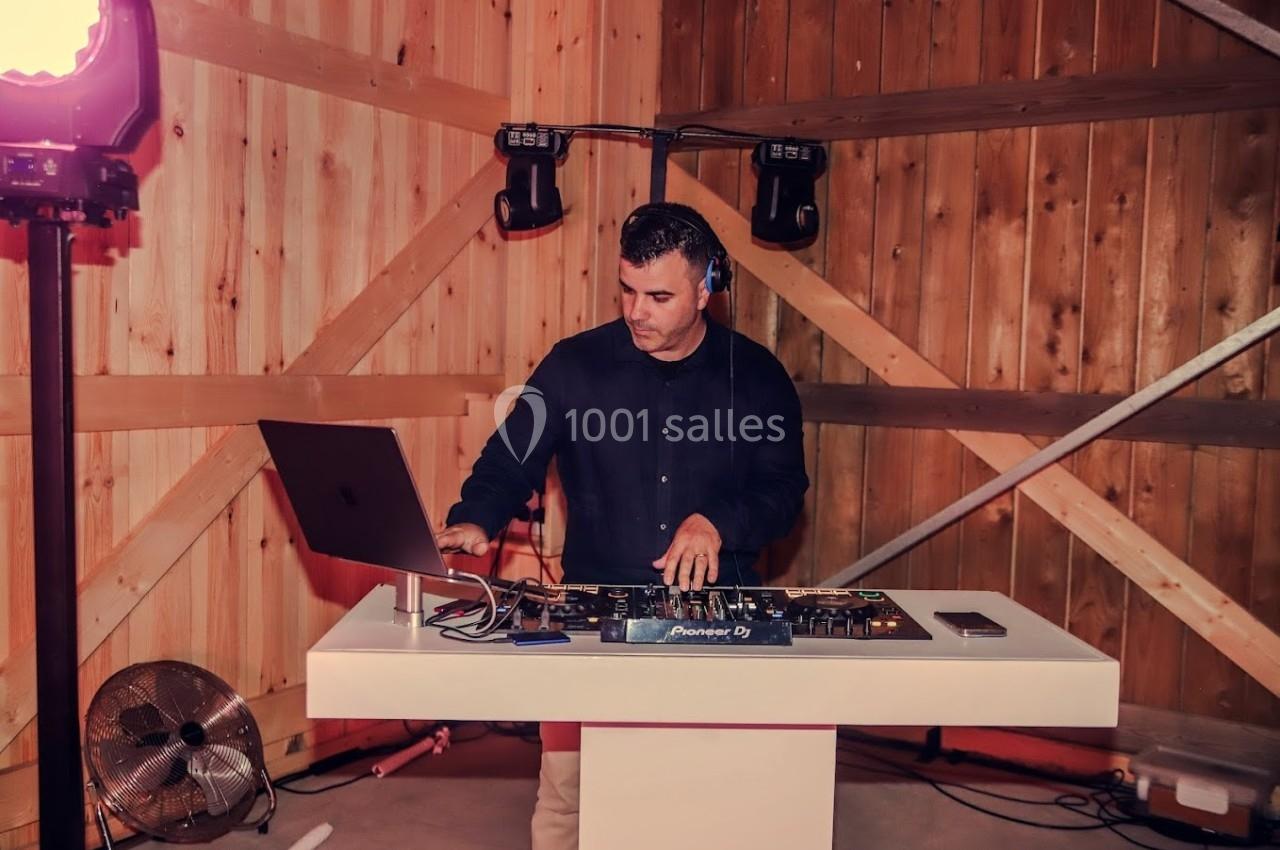 Un DJ mixe de la musique sur une table de mixage dans un espace en bois éclairé.