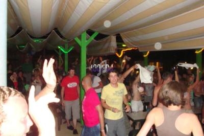 Des personnes dansent et discutent sous une tente éclairée lors d'une soirée animée.