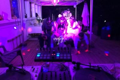 Des personnes dansent sous une tente éclairée par des lumières colorées, avec une table de mixage au premier plan.