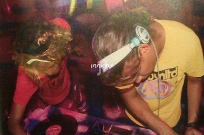 Deux DJ mixent des vinyles sur des platines dans une ambiance de club avec éclairages colorés.