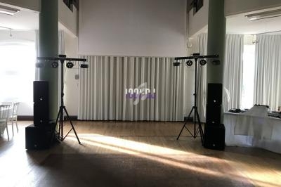 Installation de matériel audio et éclairage dans une salle lumineuse avec rideaux blancs et parquet en bois.