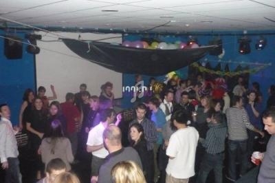 Des personnes dansent et discutent dans une salle décorée avec des ballons et des guirlandes.