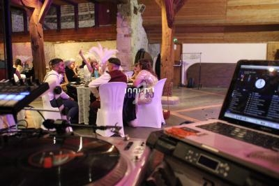 Vue d'une salle de réception avec des invités assis, un DJ en arrière-plan et du matériel audio au premier plan.