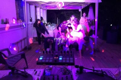 Des personnes dansent et s'amusent sous une tente éclairée de lumières colorées, avec une table de mixage au premier plan.