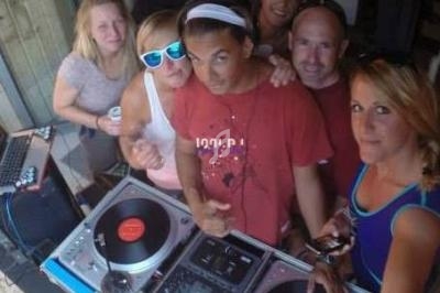 Un groupe de personnes pose autour d'une table de mixage avec des platines vinyles en extérieur.