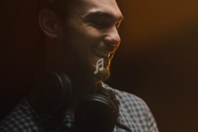 Homme souriant dans une lumière tamisée, portant un casque audio autour du cou.