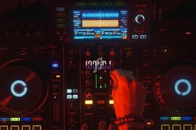 Main d'une personne ajustant les réglages sur une console de mixage DJ illuminée avec des écrans et des boutons colorés.