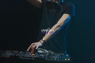 Un DJ en t-shirt noir mixe de la musique sur une table de mixage dans une ambiance sombre.