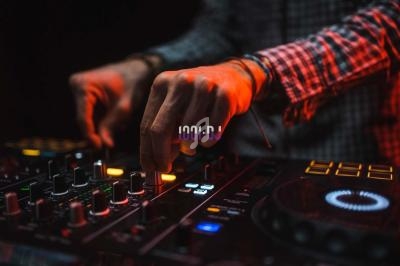 Main ajustant des commandes sur une table de mixage DJ éclairée par une lumière rouge dans un environnement sombre.