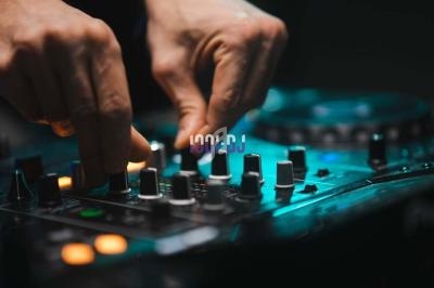 Mains ajustant les réglages sur une table de mixage audio éclairée dans une ambiance sombre.