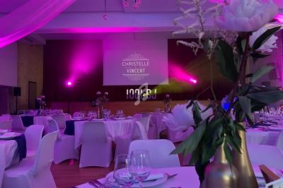 Salle de réception décorée avec des fleurs, éclairage rose et écran projetant des noms en arrière-plan.