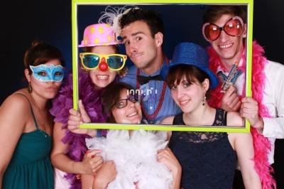 Un groupe de personnes déguisées avec des accessoires festifs pose en tenant un cadre coloré.