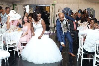 Un couple de mariés danse au milieu des invités assis dans une salle de réception décorée.