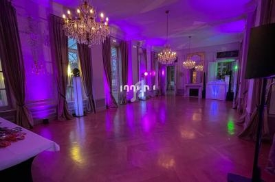 Salle élégante avec parquet, lustres, rideaux et éclairage violet, préparée pour un événement ou une réception.