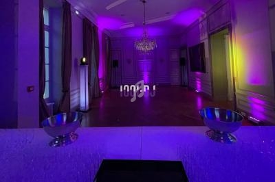 Salle de réception vide éclairée par des lumières violettes et jaunes, avec un bar au premier plan.