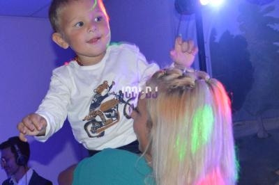 Un enfant souriant est porté par une femme dans une ambiance festive avec des lumières colorées.