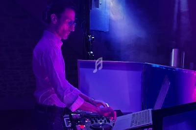 Un DJ mixant de la musique sur une console éclairée par des lumières violettes dans une ambiance sombre.