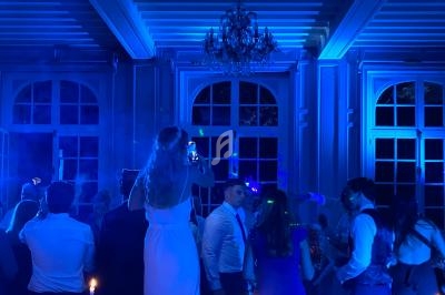 Groupe de personnes dans une salle éclairée de lumières bleues, une femme en robe blanche prend une photo.