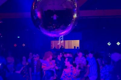 Des personnes dansent sous une boule à facettes dans une ambiance lumineuse bleutée.