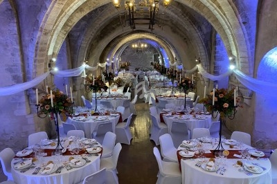 Salle voûtée décorée pour un banquet, avec tables rondes dressées, chandeliers et éclairage tamisé.