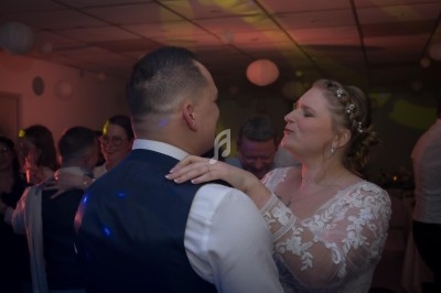 Un couple danse lors d'une réception, entouré d'invités dans une salle décorée de lanternes suspendues.