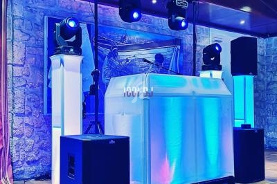 Installation de matériel de sonorisation et d'éclairage avec une table de DJ éclairée dans une salle en pierre.