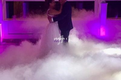 Un couple danse dans une salle éclairée de lumières violettes, entouré d'une épaisse fumée au sol.