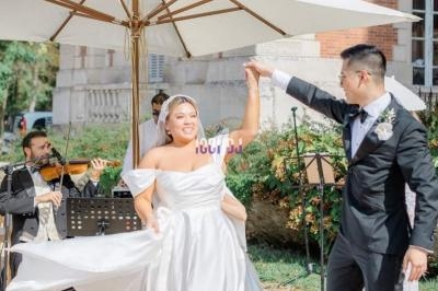 Un couple de mariés danse sous un parasol, accompagné par un quatuor à cordes en extérieur.