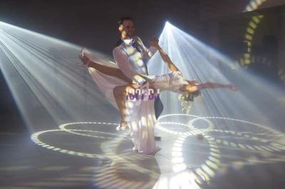 Un couple exécute une danse élégante sous des projecteurs lumineux créant des motifs circulaires au sol.