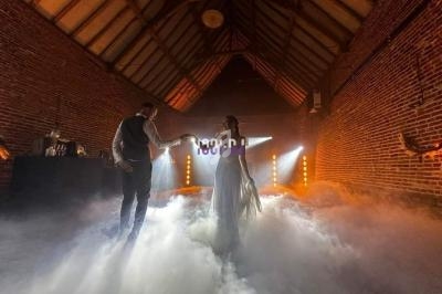 Un couple danse au milieu d'une salle en briques avec un éclairage chaleureux et un sol recouvert de fumée.